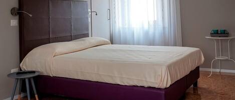 Un dormitorio con cama, una mesita y una cortina.