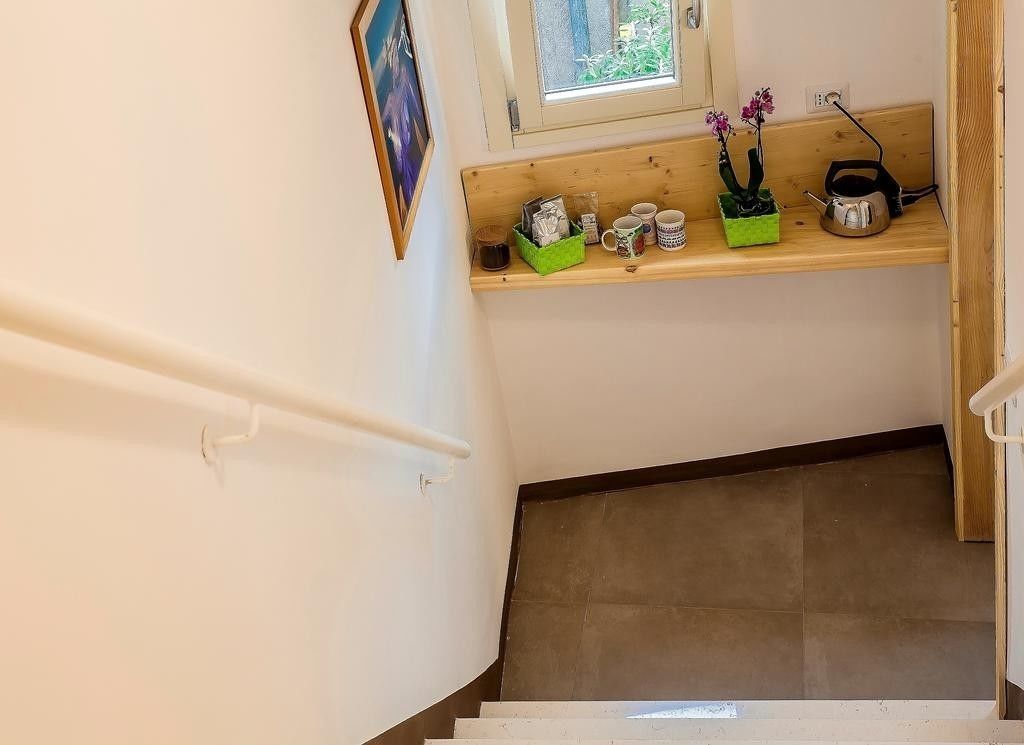 Una escalera con un estante de madera encima, donde hay una cesta verde, una planta en maceta y un hervidor.