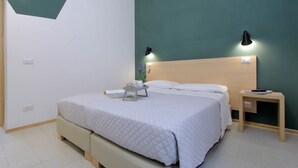 Un lit bien fait, recouvert d’une couverture matelassée, une table de chevet avec une lampe et un luminaire fixé au mur.