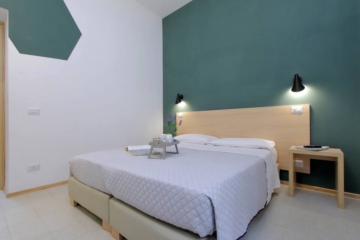 Una cama bien tendida con un edredón acolchado, una mesita de noche con una lámpara y una lámpara de pared.