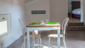 Un coin repas avec une table dressée pour deux personnes, une fenêtre et un lit en arrière-plan.