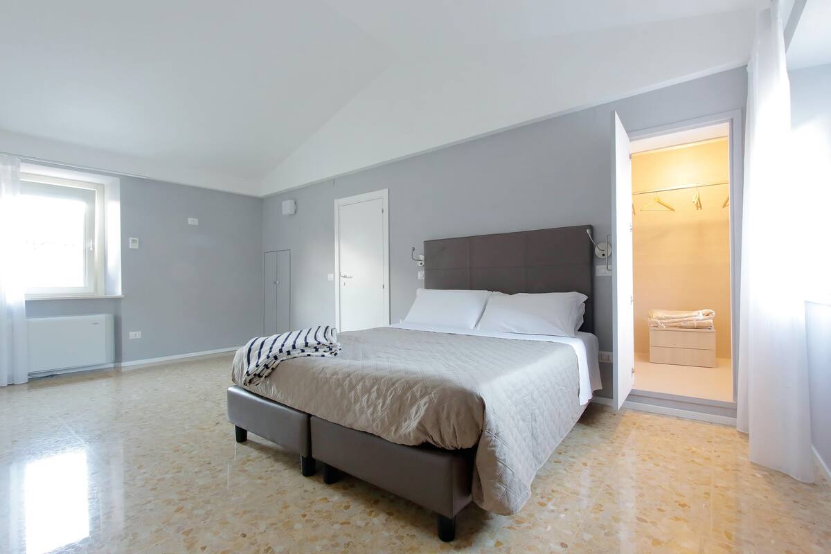 Un dormitorio con cama, mesita de noche, armario y baño visible a través de una puerta abierta.