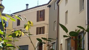Une rue étroite, bordée de bâtiments des deux côtés, avec une voiture garée et quelques plantes au premier plan.