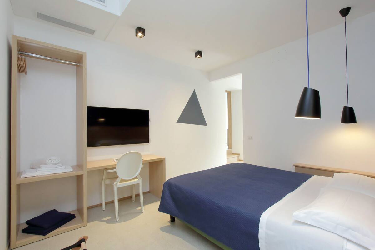 Una habitación de hotel moderna con una cama, un escritorio con una silla, un televisor y un armario.