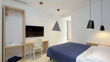 A modern hotel room with a bed, a desk with a chair, a television, and a wardrobe.