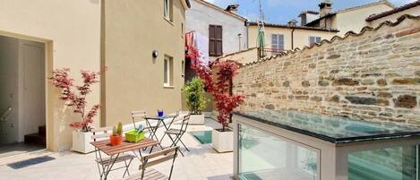 Un patio con terraza acristalada, pared de piedra y una pequeña mesa con sillas.