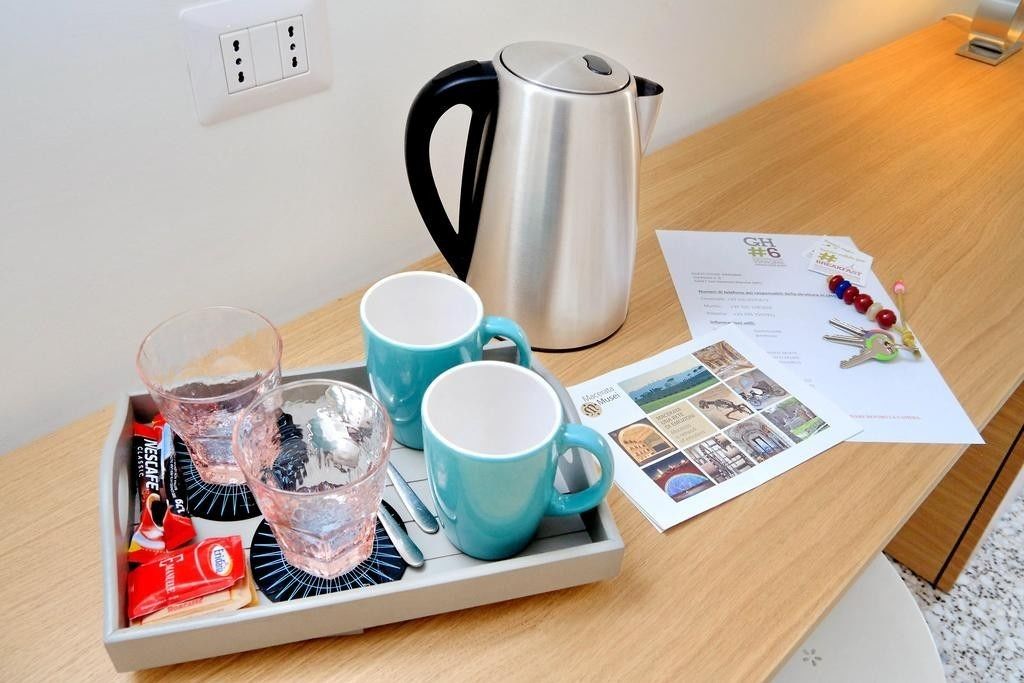 A tray with two blue mugs, a glass, and a silver kettle on a wooden table.