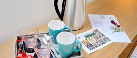 A tray with two blue mugs, a glass, and a silver kettle on a wooden table.