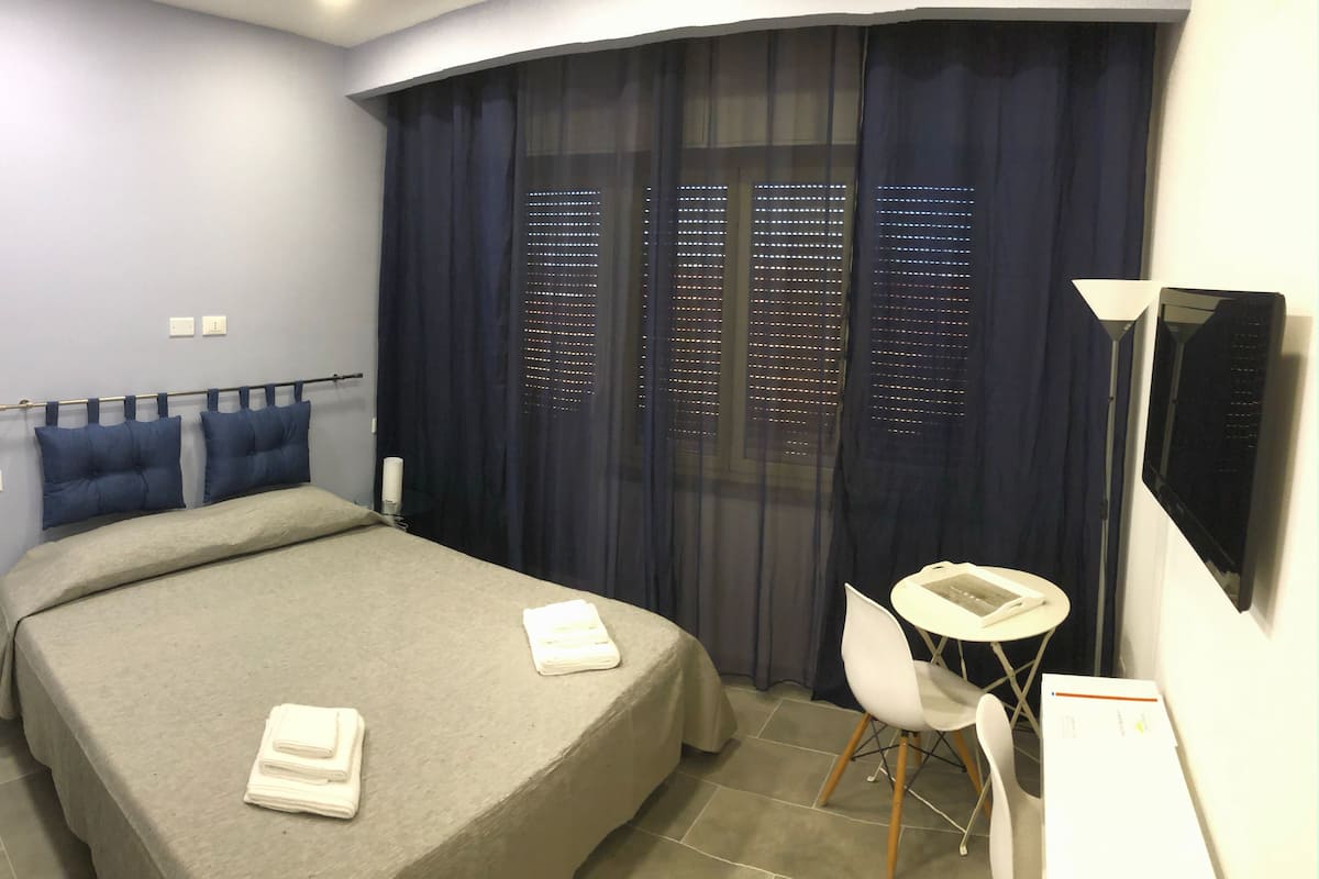 Ein Hotelzimmer mit Bett, Schreibtisch, Stuhl, Fernseher und einem Fenster mit Vorhängen.