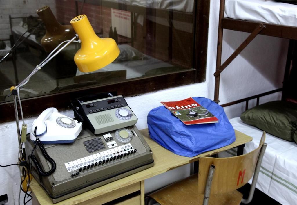 Una habitación pequeña con una cama individual superpuesta, un escritorio, un teléfono, una radio y una lámpara.
