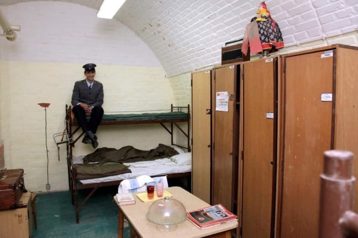 A small, compact room with bunk beds, wooden lockers, and a table with a glass dome.