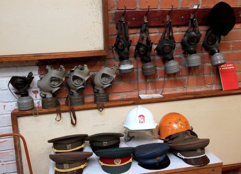 A display of military helmets and gas masks on a shelf against a brick wall.