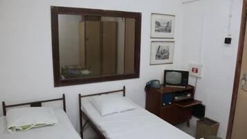 A small, simple room with two single beds, a wooden wardrobe, a television, and framed pictures on the wall.