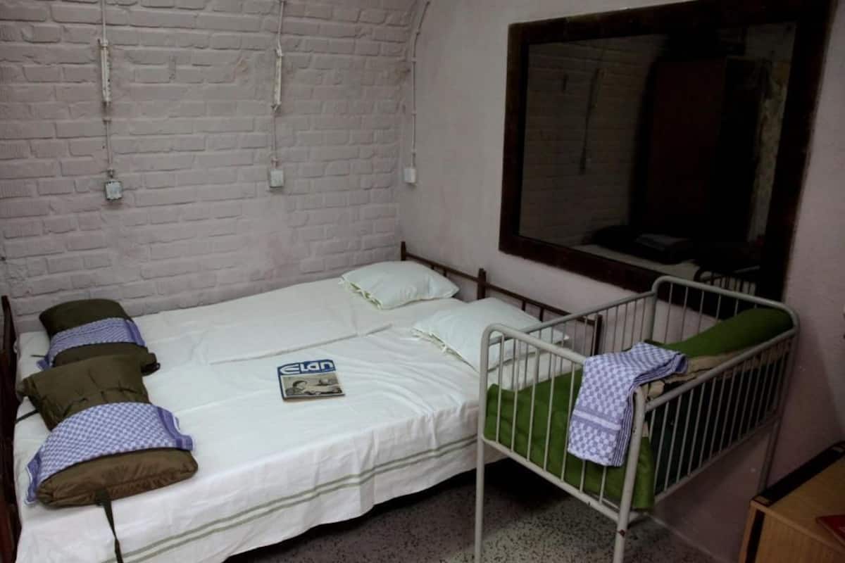 A single-bed room with a white brick wall, a window, and a metal crib.