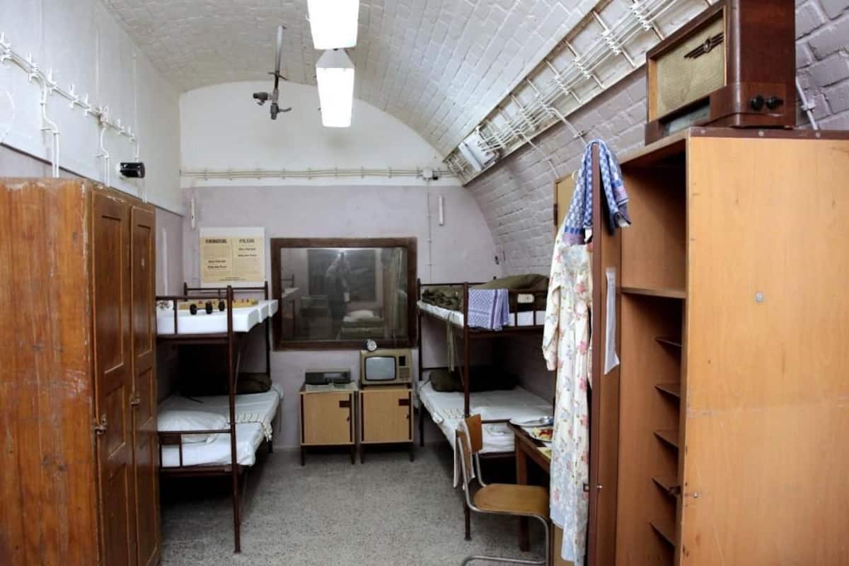 A dormitory room with bunk beds, a desk, a chair, a television, and a wardrobe.