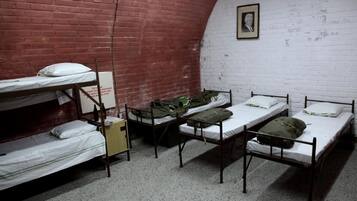Une chambre de dortoir avec des lits superposés, un mur en briques blanches et un tableau encadré accroché au mur.