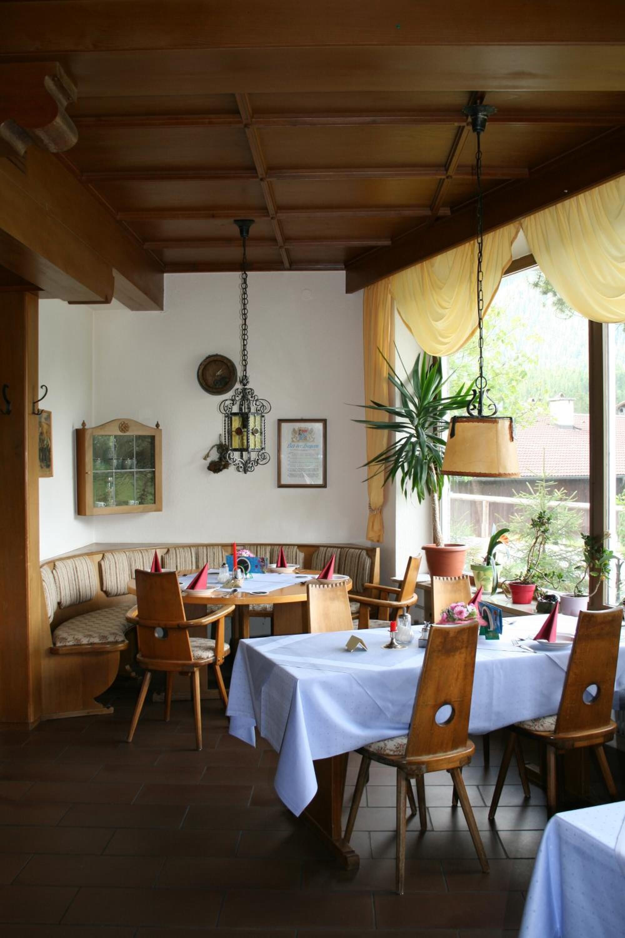 Un comedor con mesa y sillas de madera, una lámpara colgante y un ventanal con cortinas.