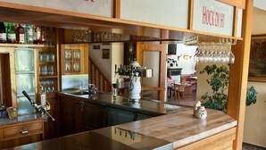 Una zona de bar con mostrador de madera, taburetes y una vitrina de vidrio.