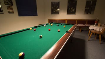 Una mesa de billar con bolas, un banco y carteles en la pared.