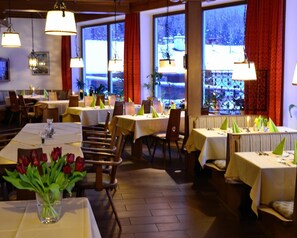 A restaurant with multiple tables, chairs, and hanging lamps. - Alpenhotel Beslhof (Ramsau bei Berchtesgaden)
