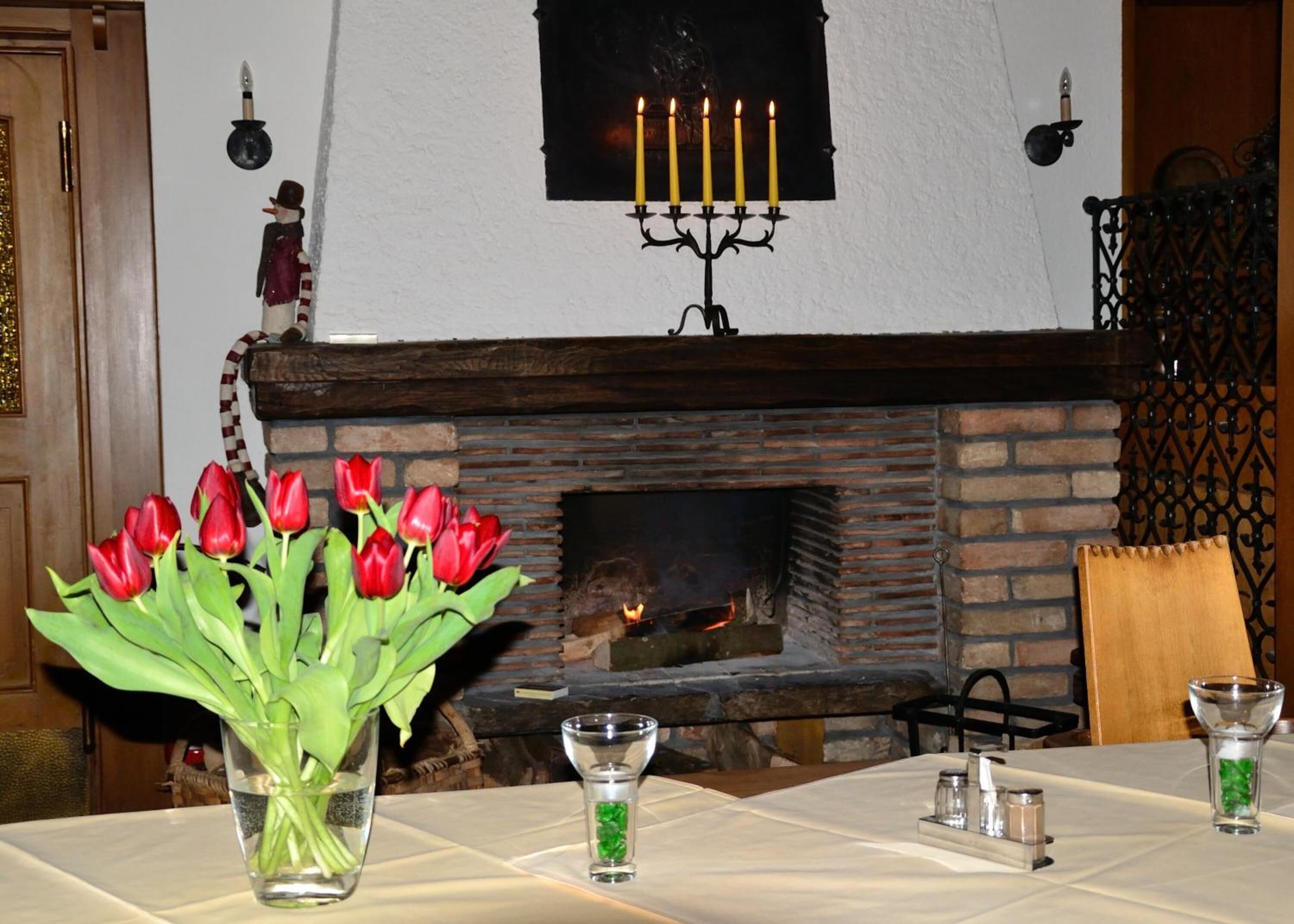 Un comedor con chimenea de ladrillo, un candelabro con velas encendidas y un jarrón con tulipanes rojos sobre la mesa.