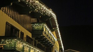 Un hotel con un balcón decorado con luces de cuerda, un comedor con mesas y sillas, y un árbol de Navidad.