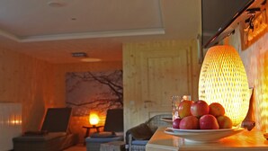 Una sala de estar acogedora con piso de madera, un sofá, una mesa con fruta y una lámpara.