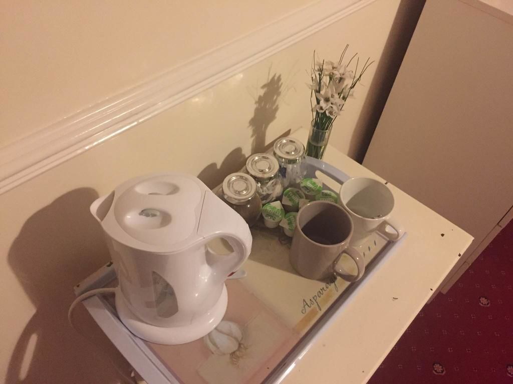 A kitchenette with a coffee maker, a tea pot, a vase with flowers, and a tray with cups and a jar.
