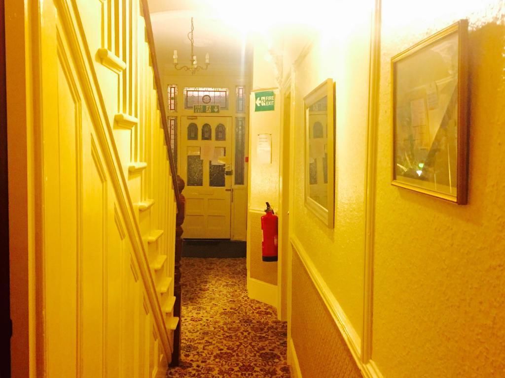 A narrow hallway with a carpeted floor, a fire exit sign, and a fire extinguisher mounted on the wall.