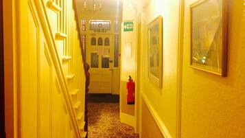 A narrow hallway with a carpeted floor, a fire exit sign, and a fire extinguisher mounted on the wall.