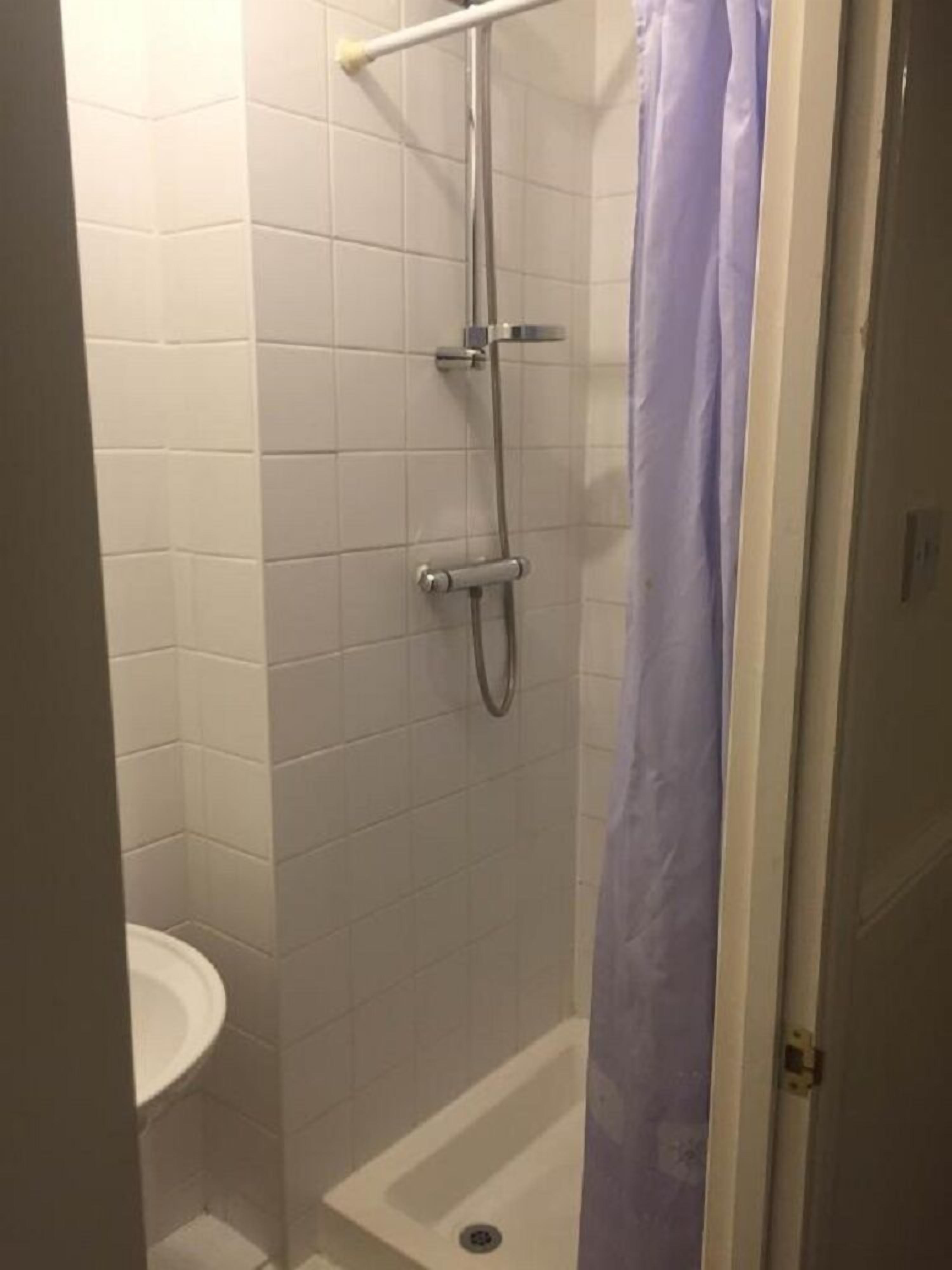 A small, enclosed shower area with a white tiled wall, a showerhead, and a handheld shower attachment.