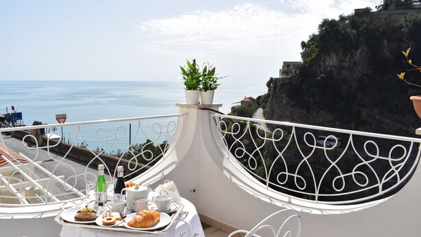 Un balcon avec une table dressée pour le petit-déjeuner, offrant une vue sur la côte.