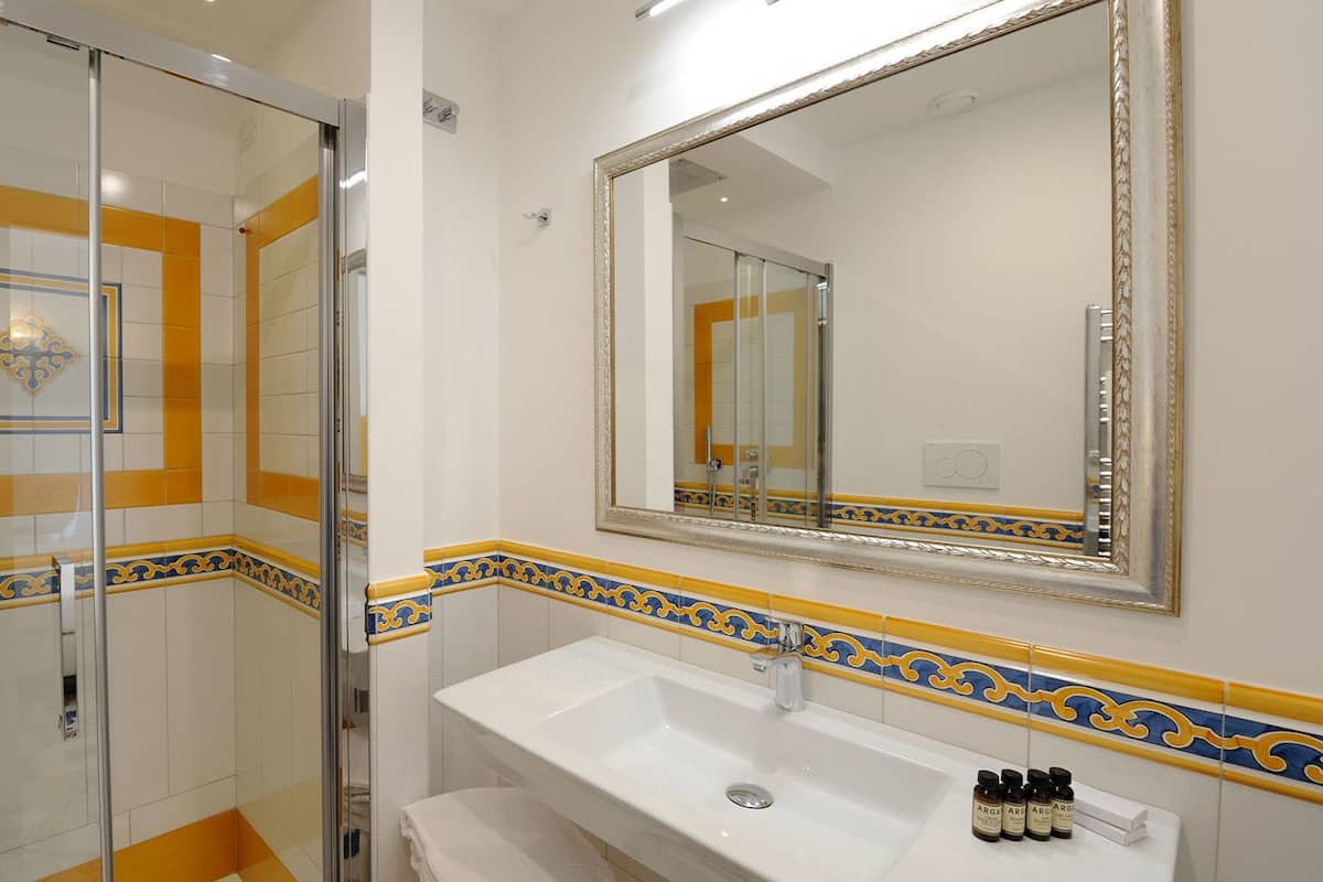 Une salle de bain dotée d’une douche à parois de verre, d’un lavabo blanc et d’un grand miroir orné d’un cadre décoratif.