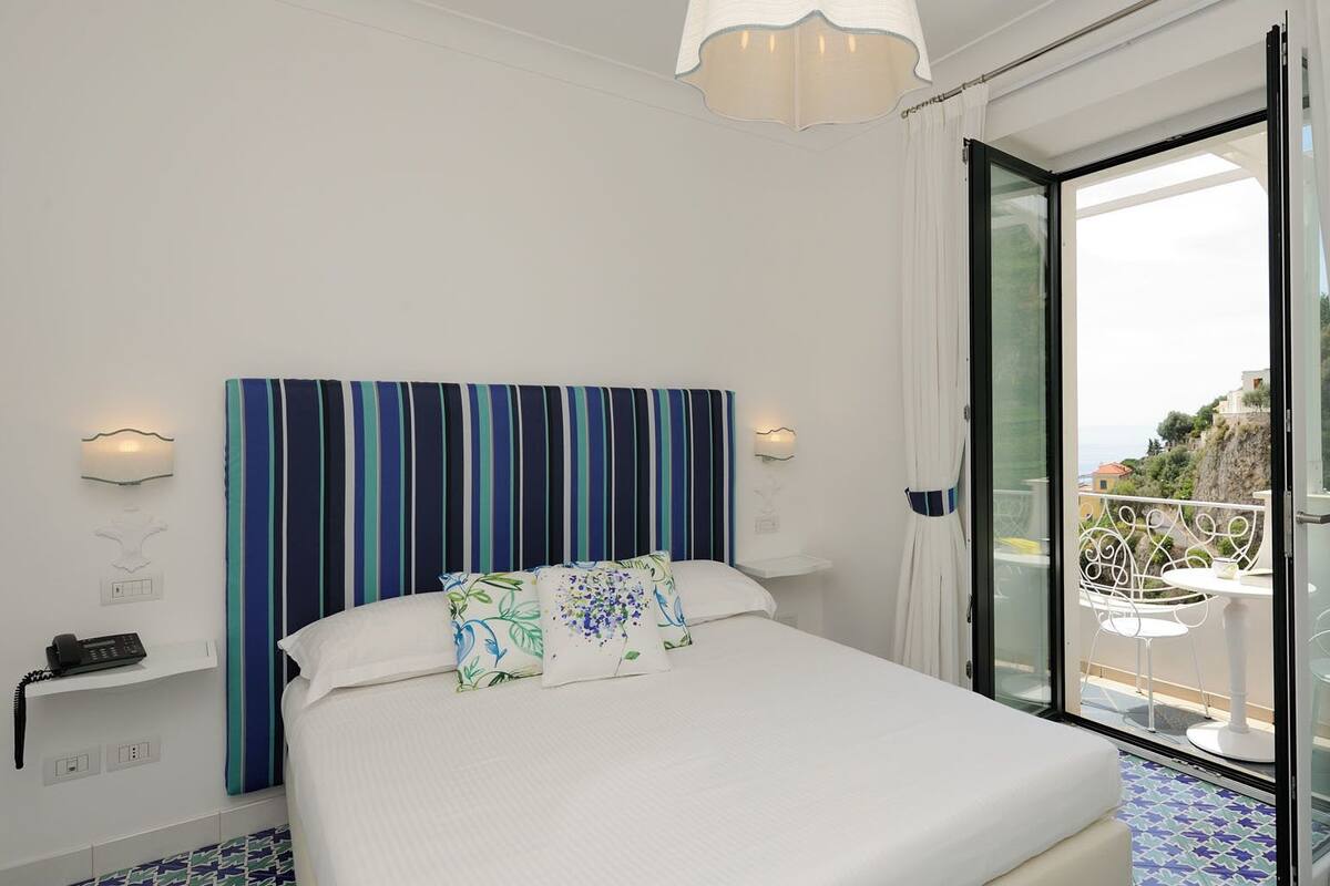 Une chambre à coucher comprenant un lit, une table de chevet, un téléphone et donnant sur l’extérieur grâce à une porte vitrée.