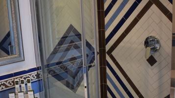 Un baño con cabina de ducha de vidrio, un lavamanos blanco con artículos de aseo y una pared de azulejos estampados.