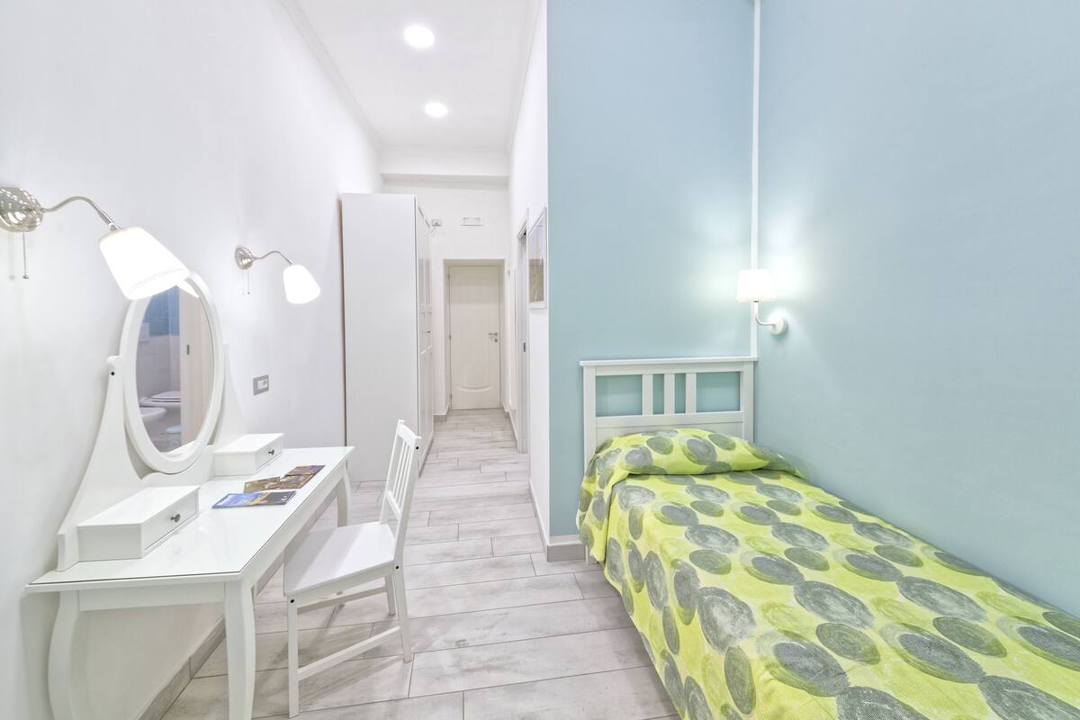 A bedroom with a bed, a desk with a mirror, and a chair.