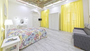 A bedroom with a floral bedspread, a grey sofa, a desk with a lamp, and a TV on the wall. - B&B Rest a Napoli (Naples)
