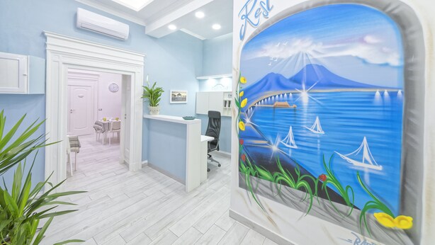 A hotel lobby with a reception desk, a dining area, and a mural of a coastal scene. - B&B Rest a Napoli (Naples)