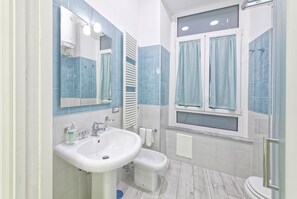 Un baño con lavamanos, bidé y ventana con cortinas.