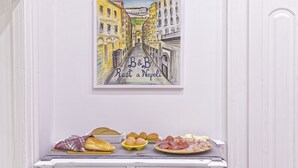 A white dresser with a framed artwork of a street scene and a breakfast spread including bread, eggs, and meats. - B&B Rest a Napoli (Naples)