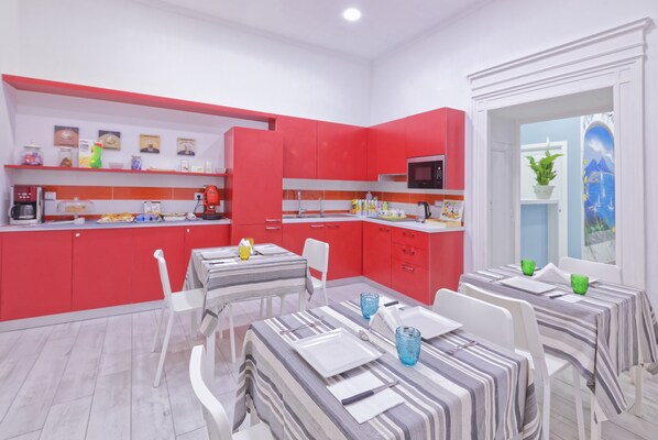 Una cocina moderna con armarios rojos, un microondas y un comedor con mantel a rayas y sillas blancas.