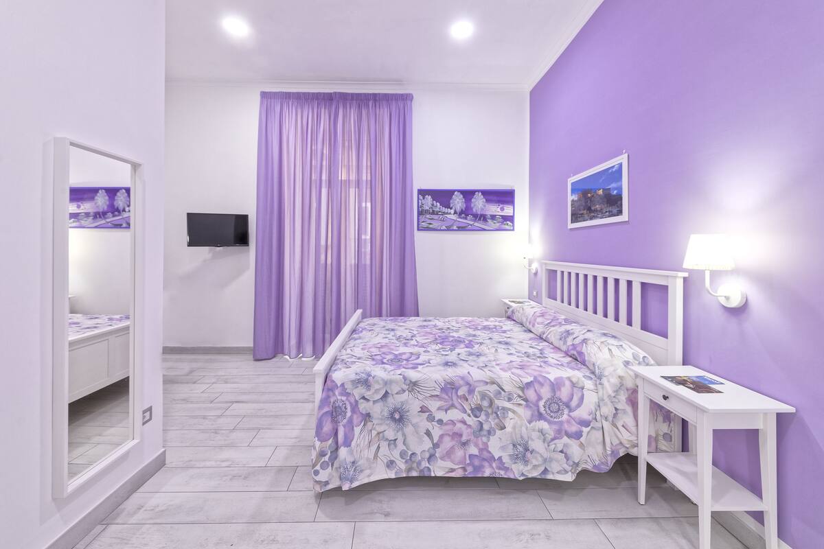 A bedroom with a bed, a bedside table, a mirror, and a TV.