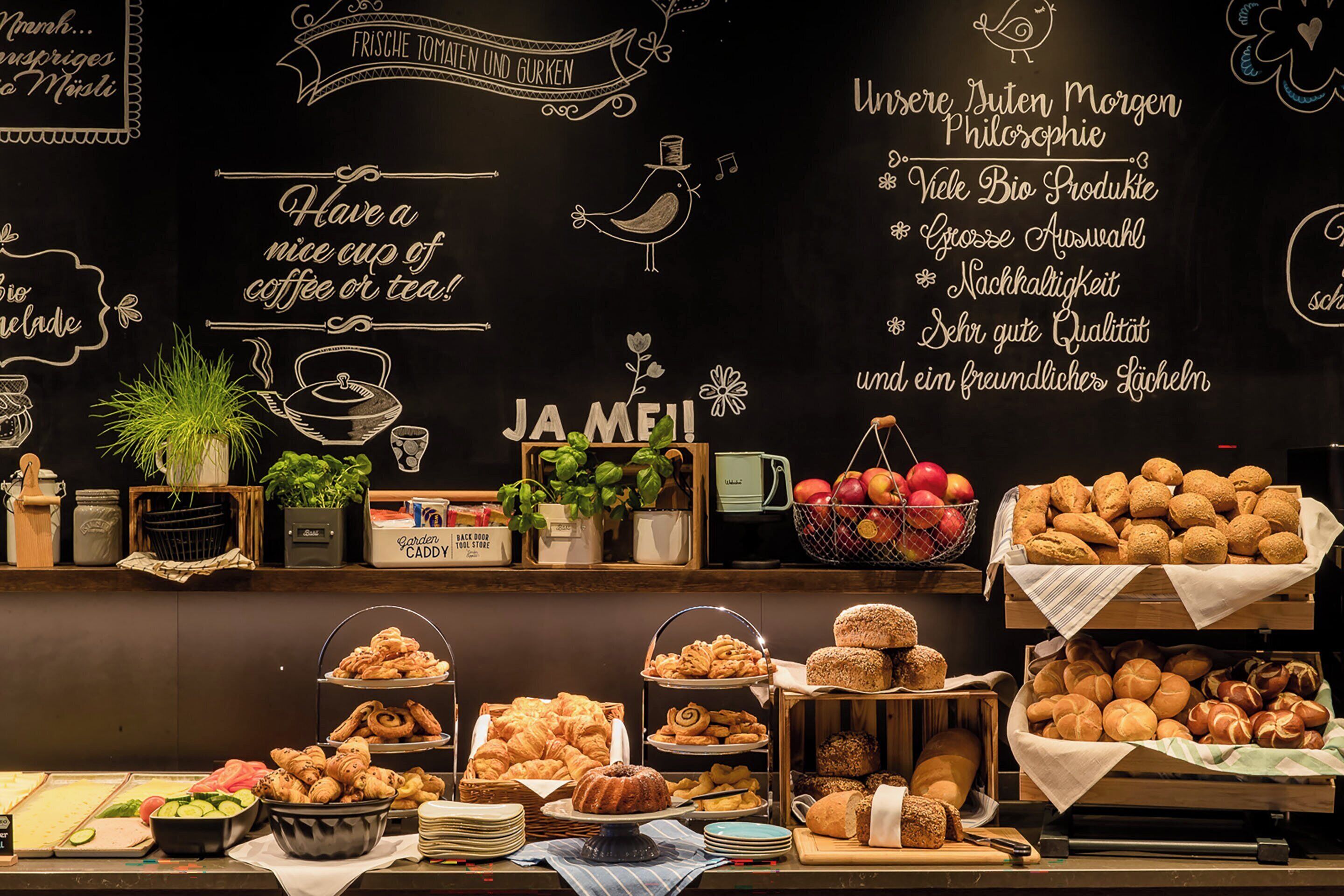 Um buffet de café da manhã com diversos pães, frutas e um quadro-negro com frases motivacionais.