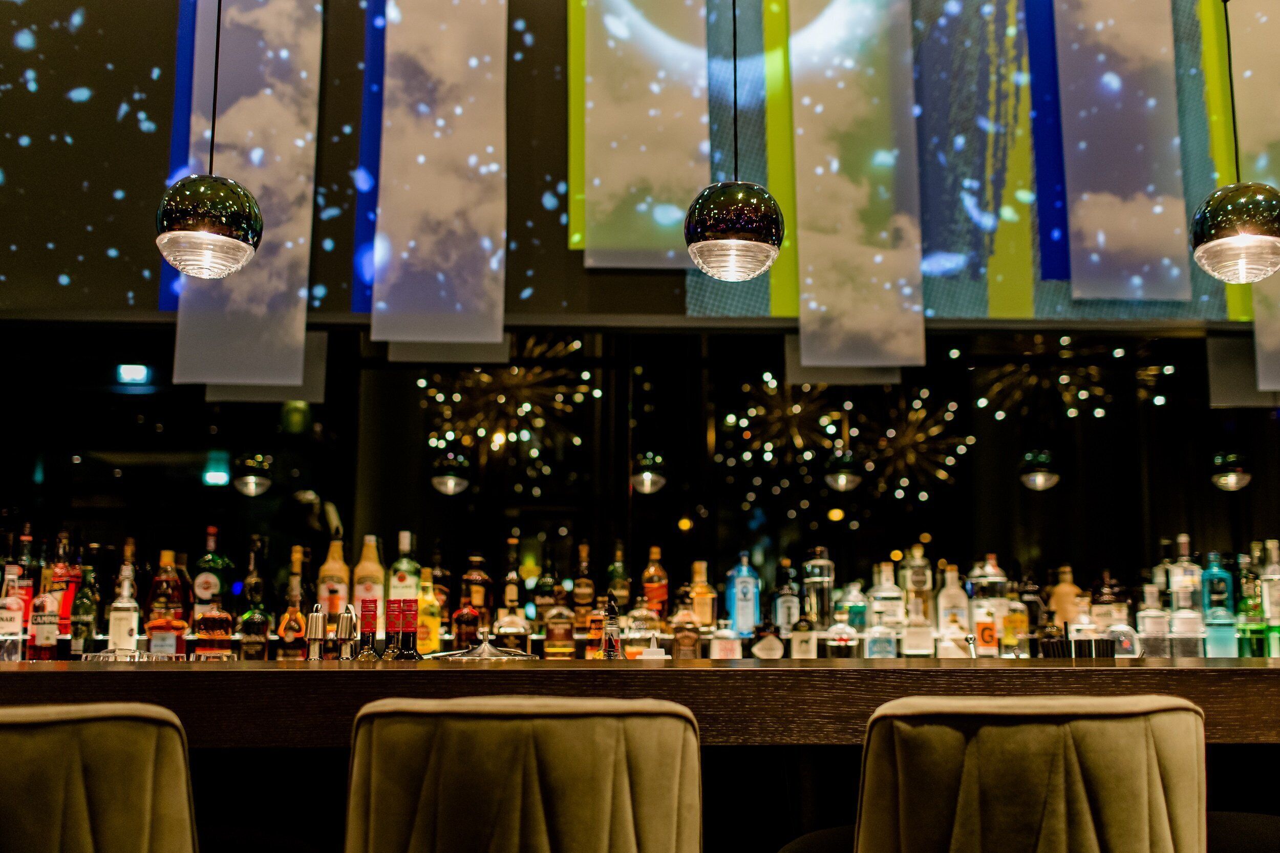 A bar area with multiple hanging lights and a variety of liquor bottles on the counter.