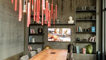 Una sala conferenze moderna con un ampio tavolo di legno, sedute confortevoli, una lavagna con note musicali, uno schermo televisivo e scaffali contenenti diversi oggetti.