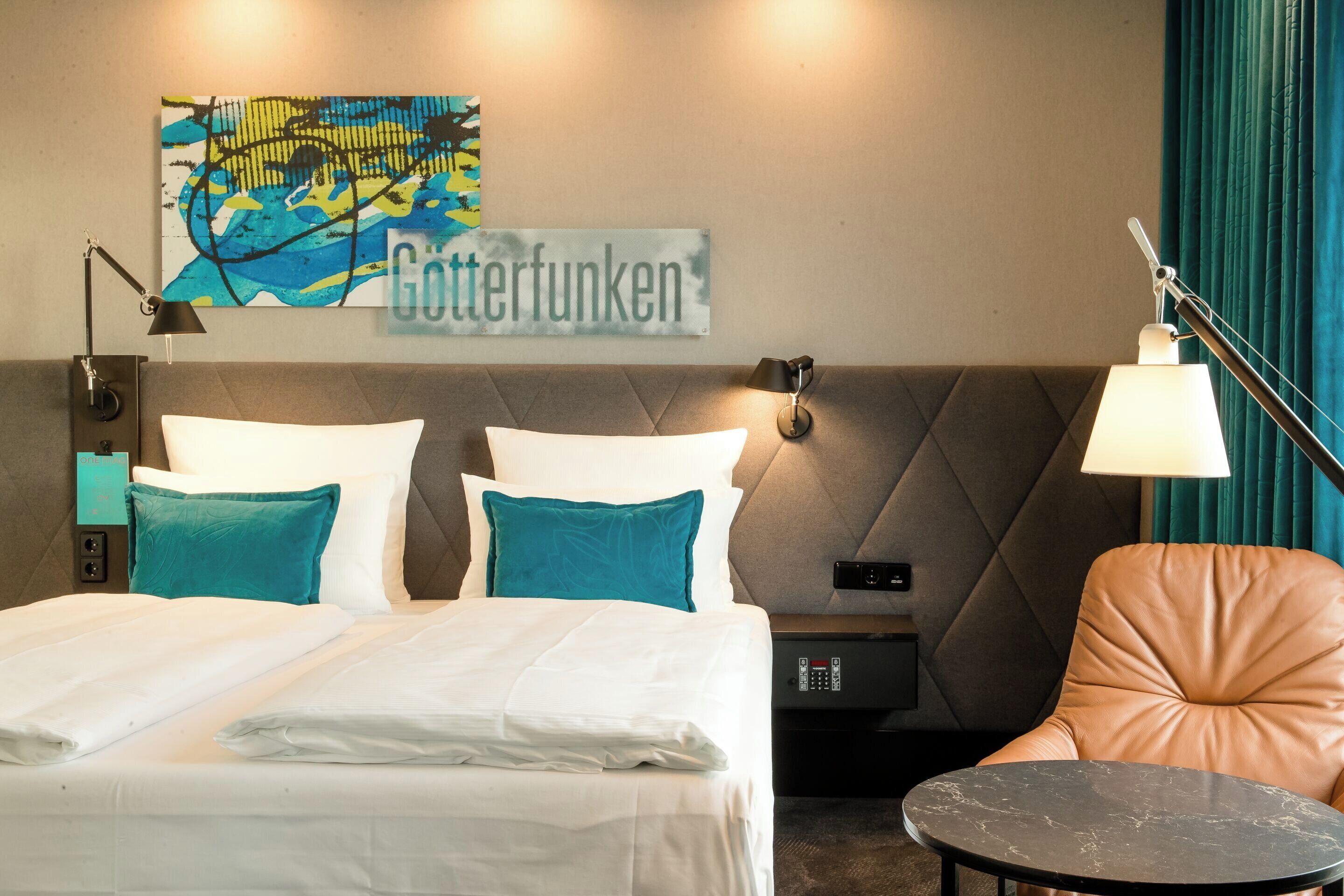 Ein Hotelzimmer mit Bett, Nachttisch, Lampe, Stuhl und einem Wandbild.