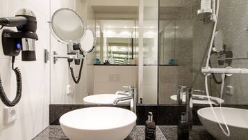 A modern bathroom with two sinks, a large mirror, a hairdryer, and a shower area.
