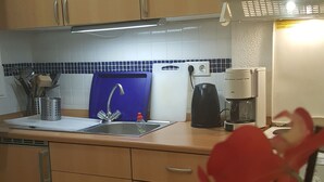 A kitchen with wooden cabinets, a sink, a coffee maker, and a blue cutting board. - Ferienhaus am Schloss Sayn (Bendorf)