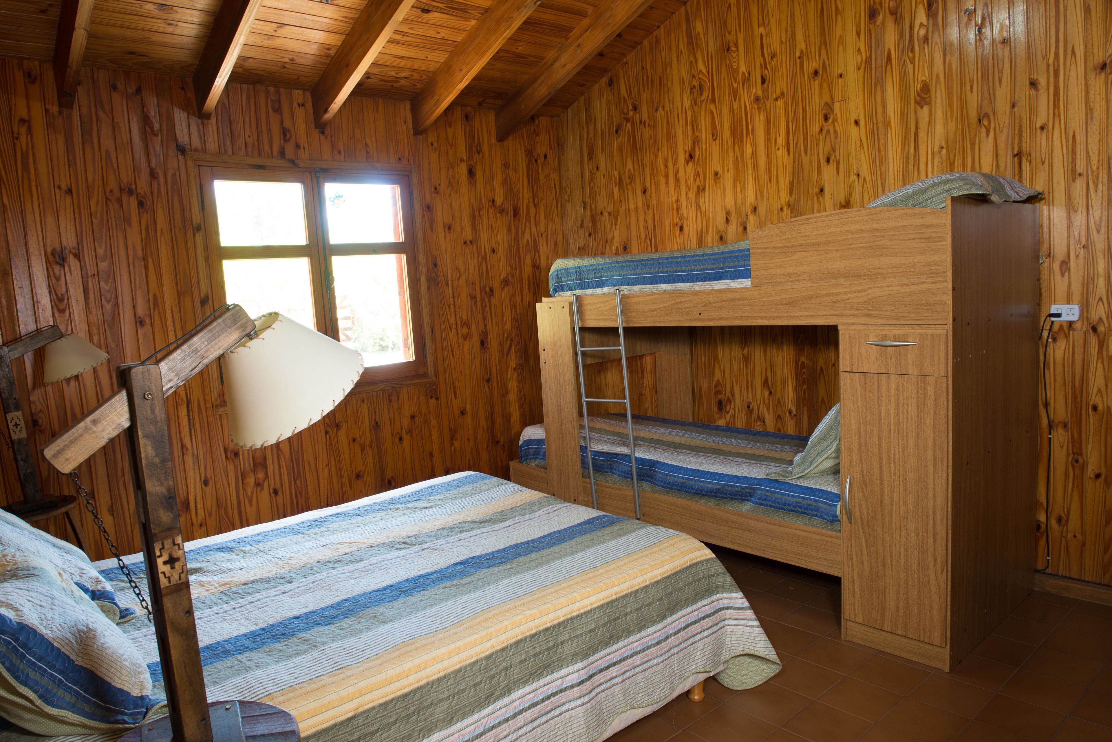 A wooden cabin room with bunk beds, a desk, and a window.