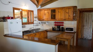 A kitchen with wooden cabinets, a white refrigerator, a stove, a microwave, and a wooden table. - Entre Montañas y Rio (Cacheuta)